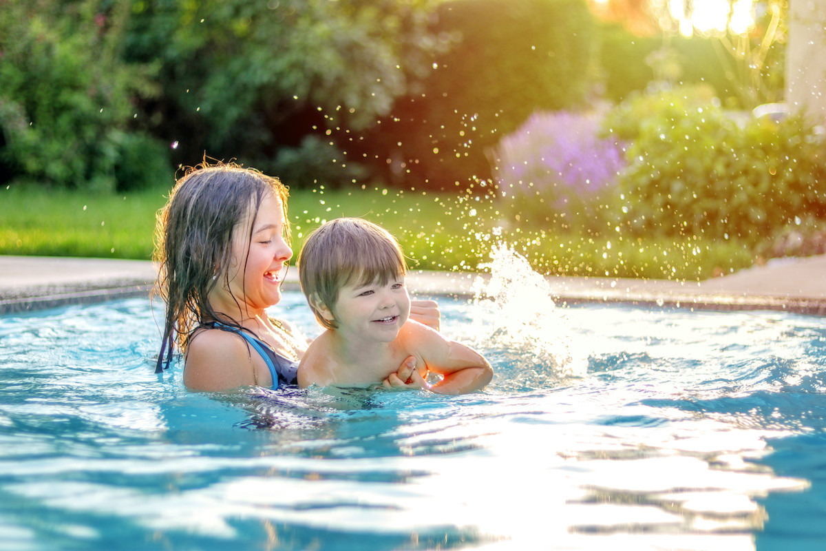 Happy siblings playing in swimming pool outdoors in garden. Preteen sister teaching her little brother to swim. Summer holidays lifestyle and leisure activity.
