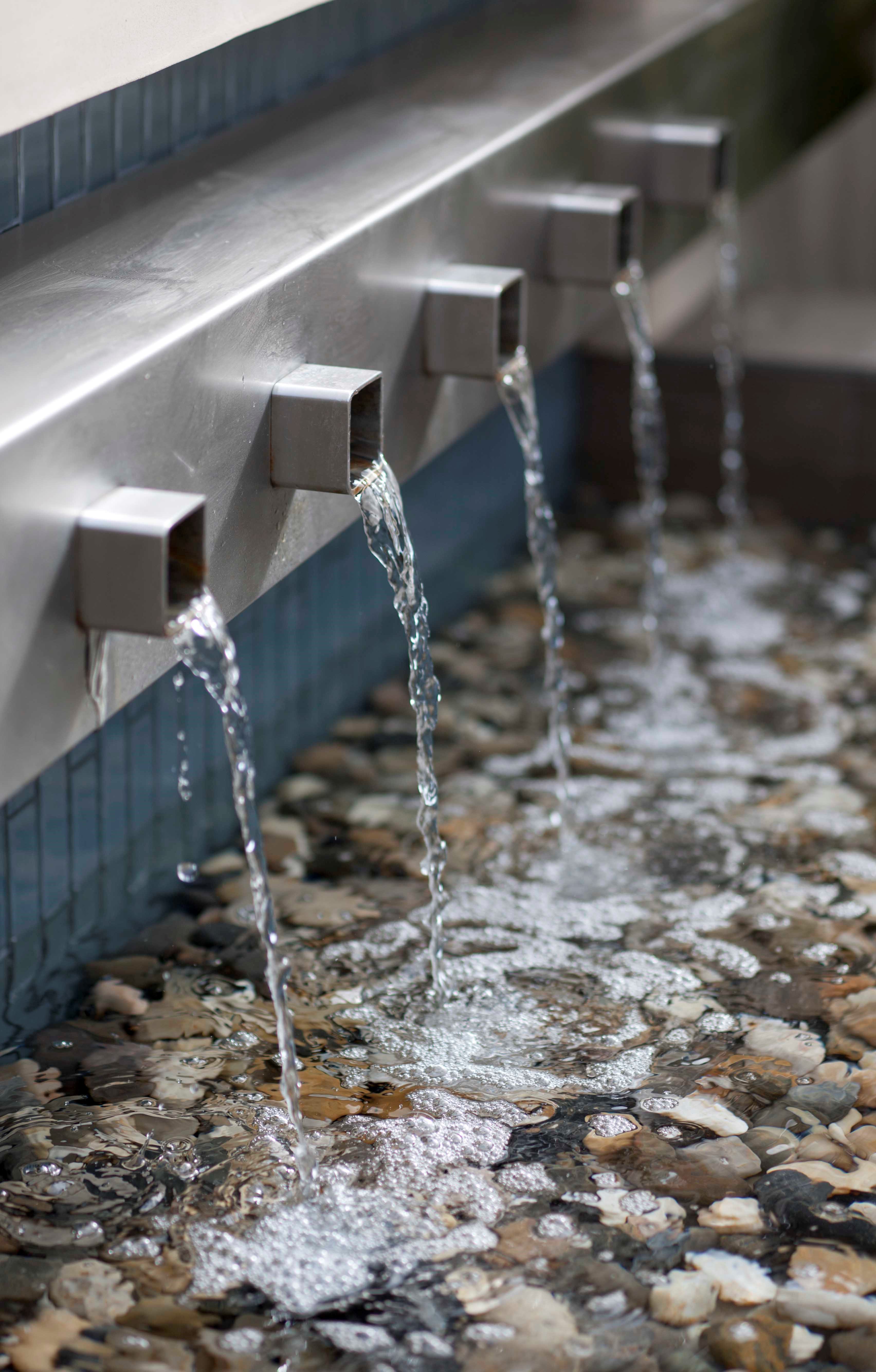 "This is a deceptive little water feature," says Kate Wiseman. "It doesn't look as hard to build as it actually is." To get the water to fall evenly from all five spouts is a physical challenge, she explains. To overcome this issue, she collaborated with the general contractor and they both came up with the idea to build a reservoir behind the spouts so that it would fill up with water first and then spill out all of the spouts simultaneously.