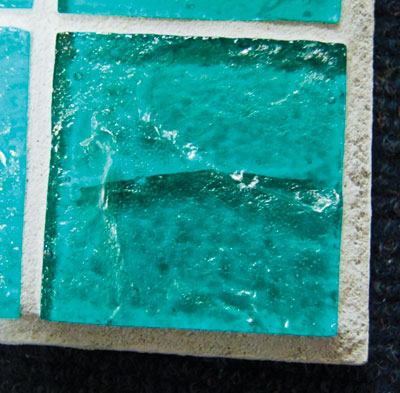 These tiles show cracks and stresses purposely induced in a manufacturer’s lab for testing. The black glass shows internal stress caused by the incorporation of incompatible raw materials. In the green tile, a thermal-shock crack developed when staff brought the tile to a high temperature, then soaked it in cold water. On an actual installation, these cracks generally are clean and run all the way through the tile. The purple glass has experienced a strain during annealing, a process by which cooling is controlled. Each glass formula has its own annealing point, which must be observed to avoid these stresses.