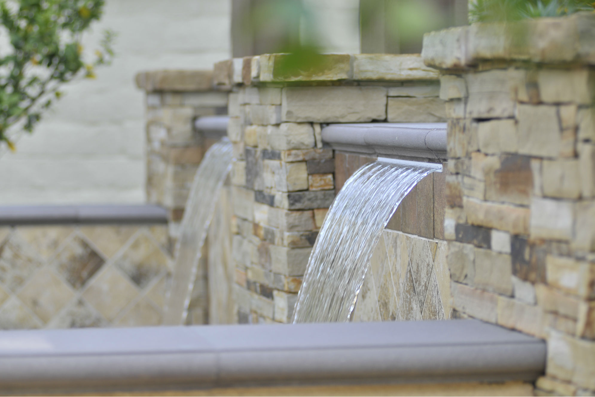 The natural hues of this design by Conscious Environments can be found in the project's stone and precast coping, the banding on the decorative perimeter details, and the pool’s porcelain tile interior and iridescent glass tile trim.