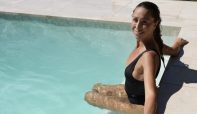 A woman in a black swimsuit sits on the edge of a pool, enjoying the sun and the water.