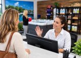 Receptionist gesturing while speaking with a customer at a pool and spa showroom desk.