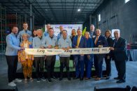 Group poses at a warehouse ribbon-cutting ceremony behind a branded white ribbon.
